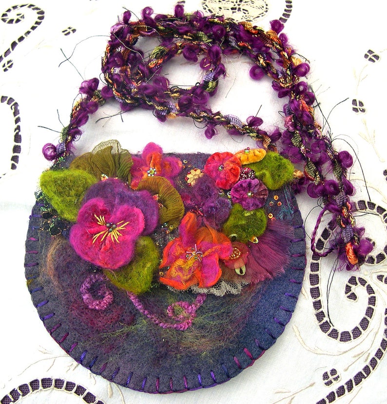 May include: A purple felt handbag with a beaded strap and floral embellishments. The bag is decorated with felt flowers in shades of pink, purple, green, and orange.