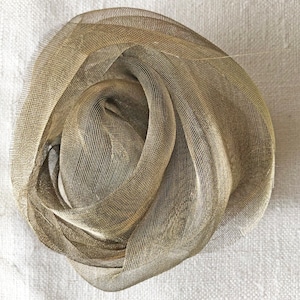 Pode incluir: Um tecido de malha dourado é reunido em uma forma circular, criando uma textura macia e delicada.