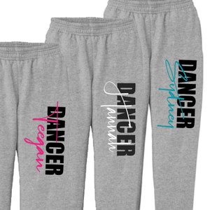 May include: Two pairs of gray sweatpants with the word "DANGER" printed on the side. One pair has the word "Dancer" written in white cursive and the other has the word "Sydney" written in blue cursive.