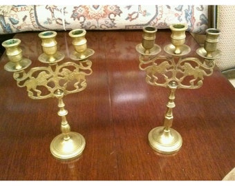 Può includere: Un paio di candelabri antichi in ottone con un design a leone. Ogni candelabro ha quattro portacandele e una base decorativa.