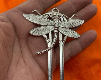May include: Silver dragonfly hair clip with intricate details. The dragonfly is perched on a pair of silver hair forks.