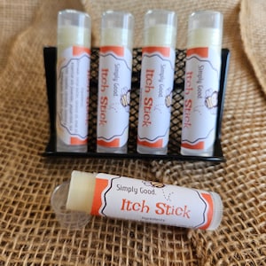 May include: Five white tubes of itch relief balm with orange labels that say "Simply Good. Itch Stick" and a small bee illustration. One tube is lying on a brown burlap surface.