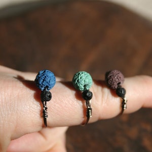 May include: Three rings with unique designs. Each ring features a small, textured, spherical bead in blue, green, and purple, paired with a smaller black bead. The beads are set on a silver-colored wire ring.