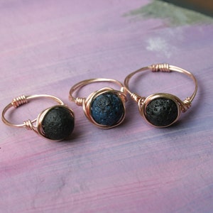 Puede incluir: Tres anillos envueltos en alambre con cuentas de roca volcánica. Los anillos están hechos con alambre de oro rosa y presentan cuentas de roca volcánica negras y azules.