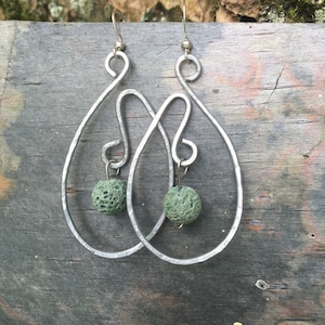 Puede incluir: Pendientes de plata con una cuenta de lava verde en cada pendiente.