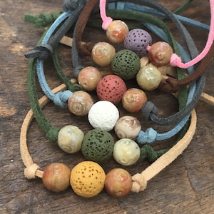 May include: A set of six bracelets with different colored suede cords and lava rock beads. The beads are a mix of natural stone and lava rock, with colors including brown, white, green, yellow, and red.