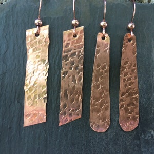 May include: Three pairs of hammered copper earrings with a textured finish. The earrings are all different shapes, with one pair being rectangular, one pair being oval, and one pair being a more rounded rectangle.