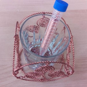 May include: A glass cup with a copper wire holder. The cup is filled with a clear glass tube with a blue cap. The tube is filled with a copper wire.