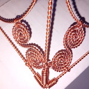 May include: A copper wire sculpture with a triangular base and three spiraled wire loops at the top.