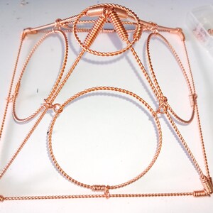 Op de afbeelding: Een koperen draadframe met een cirkelvormig ontwerp. Het frame is gemaakt van gedraaid draad en heeft een geometrische vorm.
