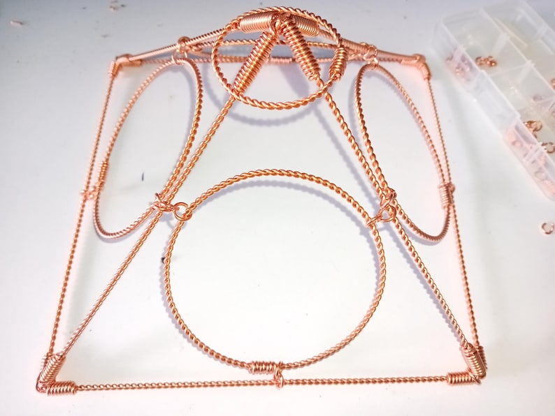 Op de afbeelding: Een koperen draadframe met een cirkelvormig ontwerp. Het frame is gemaakt van gedraaid draad en heeft een geometrische vorm.