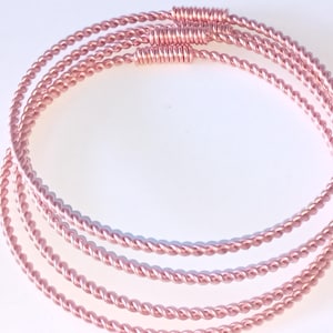 May include: Set of four rose gold colored twisted wire bangles. The bangles are stacked on top of each other.