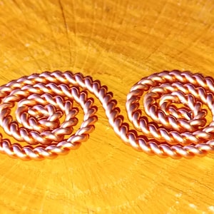 Könnte beinhalten: Zwei Kupferspiralen, jede mit mehreren Windungen, sind nebeneinander auf einer Holzoberfläche angeordnet. Die Spiralen sind rotbraun und haben eine glänzende Oberfläche.