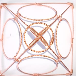Op de afbeelding: Een geometrisch beeldhouwwerk van koperdraad met een vierkante basis en vier ronde frames. Het beeldhouwwerk is gemaakt van gedraaid draad en heeft een complex ontwerp.