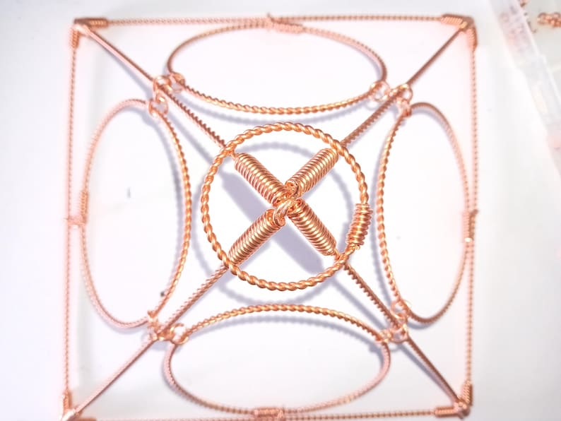 Op de afbeelding: Een geometrisch beeldhouwwerk van koperdraad met een vierkante basis en vier ronde frames. Het beeldhouwwerk is gemaakt van gedraaid draad en heeft een complex ontwerp.