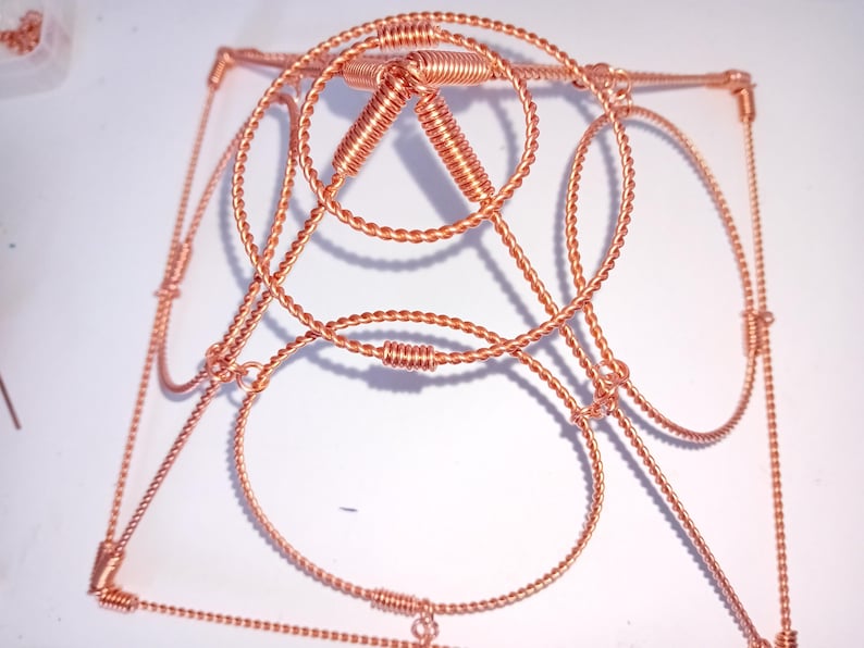 Op de afbeelding: Een sculptuur van koperdraad met een geometrisch ontwerp. Het beeldhouwwerk is gemaakt van gedraaid draad en heeft een vierkante basis met een driehoekige top.