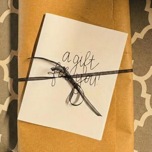 A gift wrapped in brown paper with a black ribbon tied around it, and a white card with black text on it.