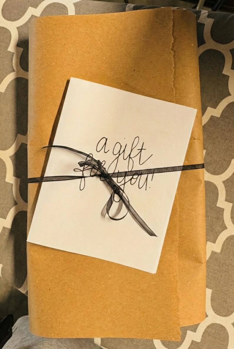 A gift wrapped in brown paper with a black ribbon tied around it, and a white card with black text on it.