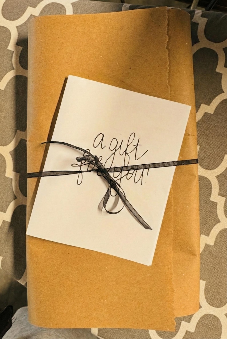 A gift wrapped in brown paper with a black ribbon tied around it, and a white card with black text on top of the paper.