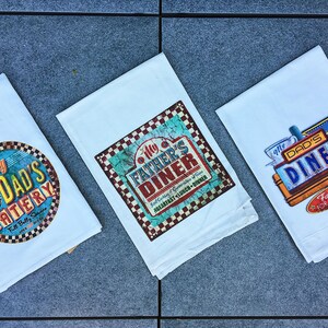 Three towels with different restaurant logos and text are laid out on a gray surface.