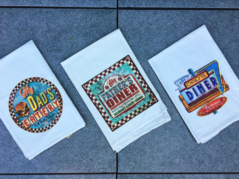 Three towels with different restaurant logos and text are laid out on a gray surface.