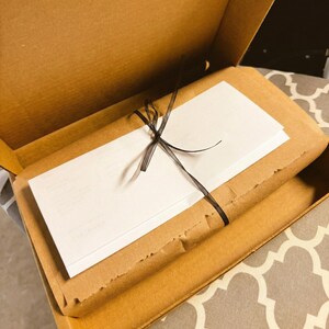 a brown cardboard box with a white card tied with a black ribbon inside it.