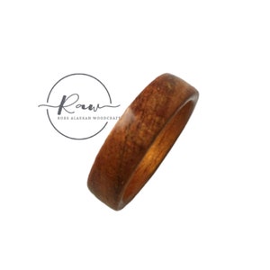 May include: A simple wooden ring with a natural brown color and a smooth finish. The ring is made from wood and has a rounded shape.