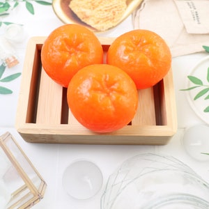 Puede incluir: Tres bombas de baño redondas de color naranja con forma de cítricos en una bandeja de madera. Las bombas de baño están dispuestas en forma de triángulo.