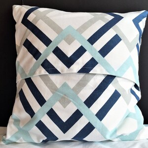 May include: A decorative pillow with a geometric pattern. The pillow features a white background with a repeating design of navy blue, light blue, and gray angled lines. The pillow is square and appears to be made of fabric.
