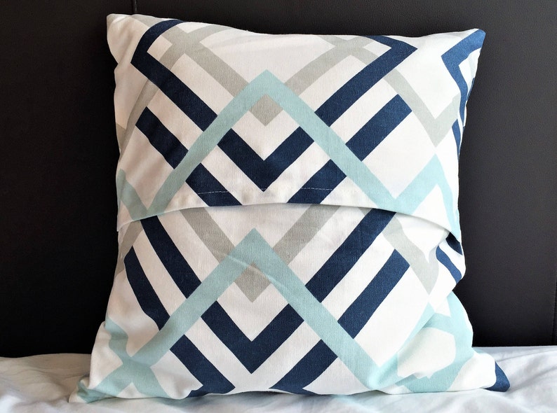 May include: A decorative pillow with a geometric pattern. The pillow features a white background with a repeating design of navy blue, light blue, and gray angled lines. The pillow is square and appears to be made of fabric.