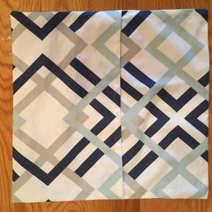 May include: Square pillow cover with a geometric pattern in navy blue, light gray, and pale blue on a white background. The design features intersecting lines and angular shapes, creating a modern aesthetic.