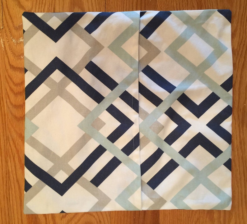 May include: Square pillow cover with a geometric pattern in navy blue, light gray, and pale blue on a white background. The design features intersecting lines and angular shapes, creating a modern aesthetic.