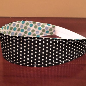 May include: A black and white polka dot headband with a white elastic band. The interior lining features a pattern of teal and green polka dots on a white background. This accessory is designed for comfort and style.