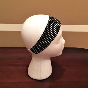 May include: A black and white polka dot headband is shown on a white mannequin head. The headband is made of fabric and has a simple design. The white polka dots are evenly spaced on a black background. The headband is approximately 5 cm wide.