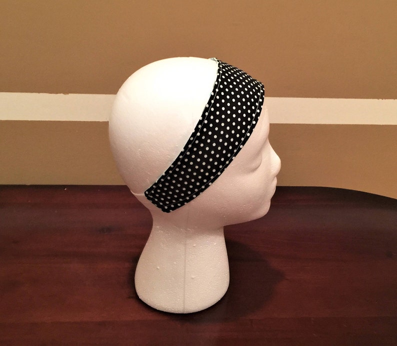 May include: A black and white polka dot headband is shown on a white mannequin head. The headband is made of fabric and has a simple design. The white polka dots are evenly spaced on a black background. The headband is approximately 5 cm wide.