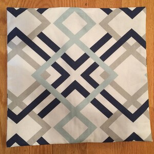 May include: Square pillow with a geometric pattern. The design features intersecting lines and shapes in navy blue, light blue, and gray against a white background. The pillow is square and appears to be made of fabric.