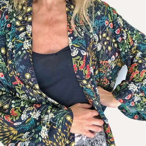 Puede incluir: Un kimono azul oscuro con estampado floral que presenta una variedad de colores, incluyendo rojo, amarillo, verde y blanco. El kimono tiene mangas largas y un cuello ancho y abierto.