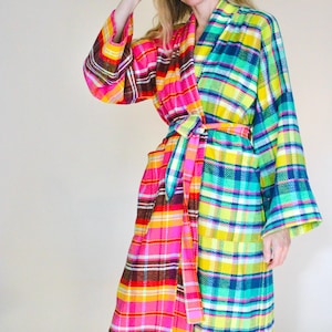 May include: A long-sleeved robe featuring a split-panel design with a vibrant plaid pattern. The left side displays bright pink, orange, and brown tones, while the right side showcases a mix of neon yellow, teal, and blue, finished with a matching tie belt.