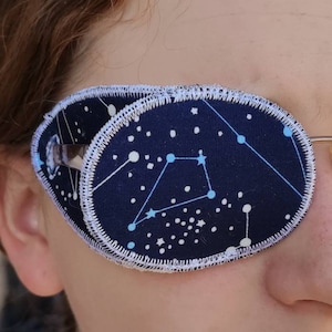 May include: A blue eye patch with a white stitched border and a constellation pattern. The patch has white and blue stars and lines connecting them.