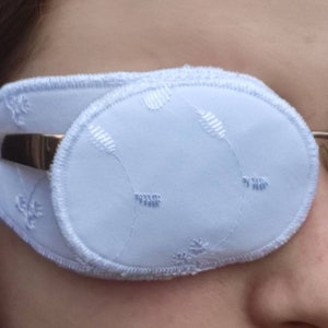 May include: A white eye patch with a delicate floral pattern. The patch is made of soft fabric and has a comfortable fit.