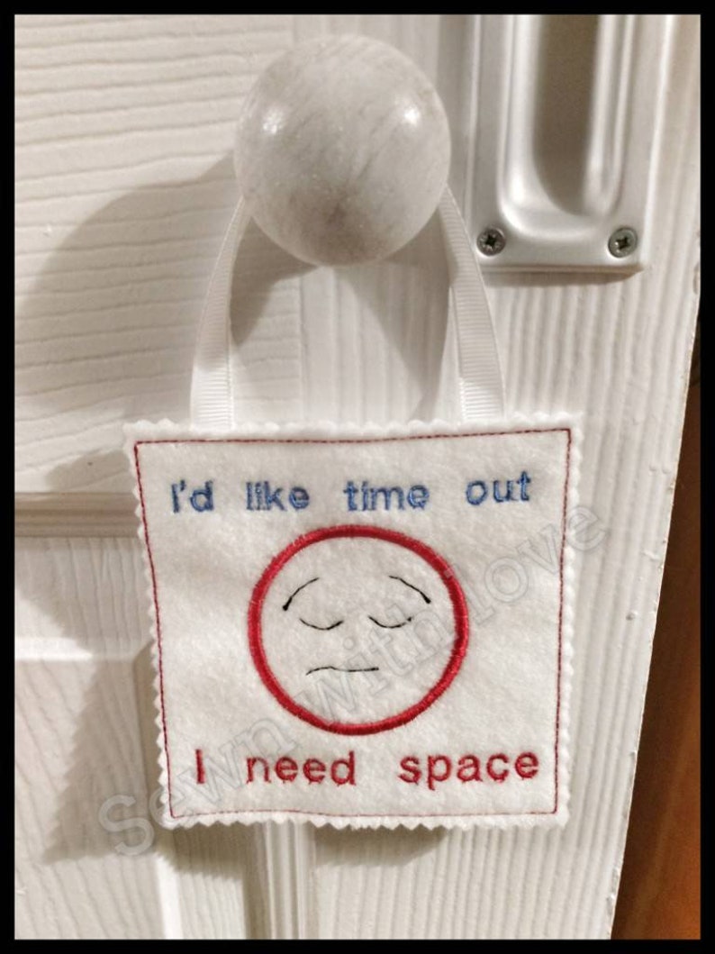 May include: White felt door hanger with red and blue embroidery. It says "I'd like time out I need space" with a sad face in a red circle.