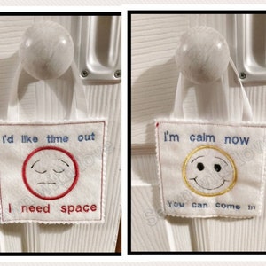 May include: Two white felt door hangers with embroidered text and smiley faces. The first hanger says "I'd like time out I need space" with a red frowning face. The second hanger says "I'm calm now you can come in" with a yellow smiling face.