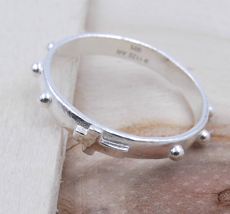 May include: Silver rosary ring with a small cross and beads. The ring is engraved with "925 ITALY".