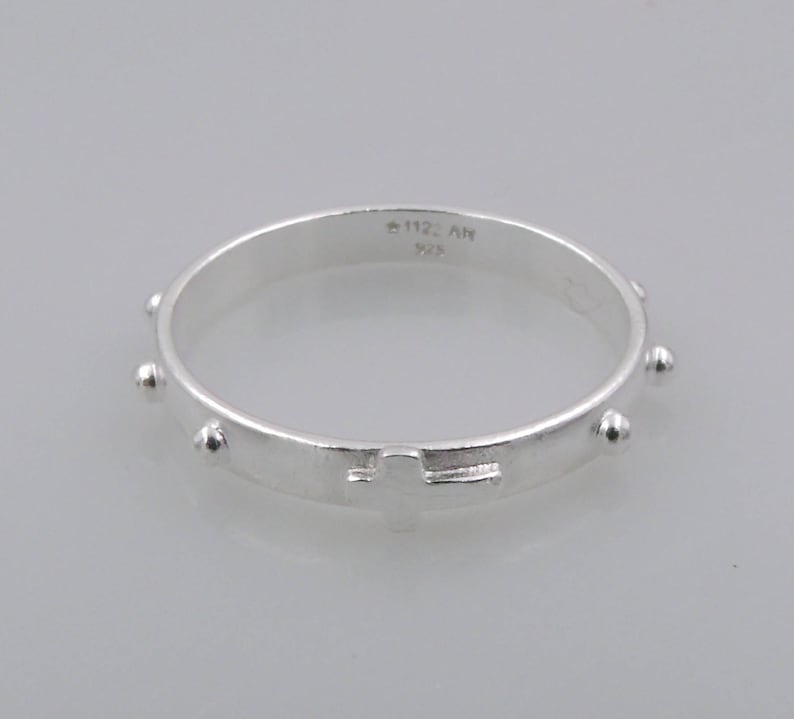 May include: Silver rosary ring with a cross and small beads. The ring is marked with "925" and "112 AN".