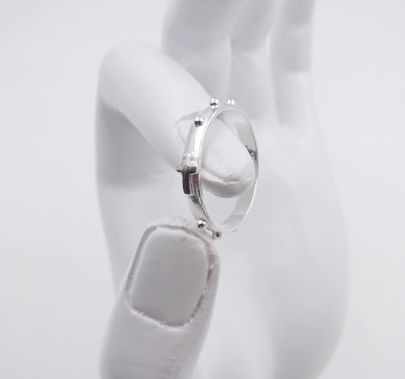 May include: A silver rosary ring with small beads and a cross.