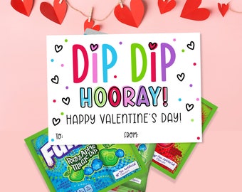 May include: A Valentine's Day card with the text "Dip Dip Hooray! Happy Valentine's Day!"  The card is white with pink, blue, and green hearts.  The card is next to a packet of Fun Dip, a powdered candy dip.