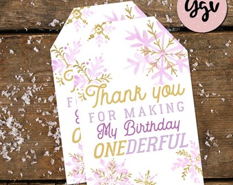 May include: Two white thank you tags with a purple and gold snowflake design. The text on the tag reads "Thank you for making my birthday onederful".
