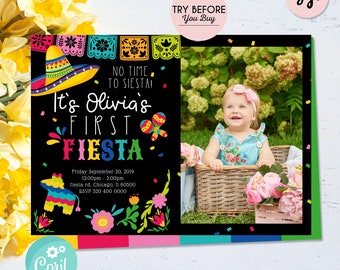 May include: A colorful invitation for a first birthday party with a fiesta theme. The invitation features a black background with colorful text that reads "It's Olivia's First Fiesta". The invitation also features a photo of a baby girl in a blue dress sitting in a wicker basket. The invitation includes the date, time, and location of the party.