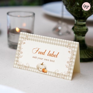 May include: A folded food label with a beige gingham border and floral accents. The words "Food label" are written in a script font, with "add your own text" below. Two small pumpkins are at the bottom.