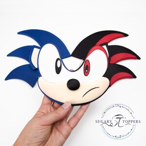 May include: A two-sided character face, featuring blue and black quills, white face, and red eyes. The character has a stern expression. The logo "Sugary Toppers" is visible in the bottom right corner.